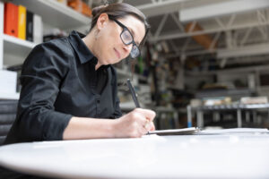 A female team member wearing glasses and a black shirt diligently sketching in an office